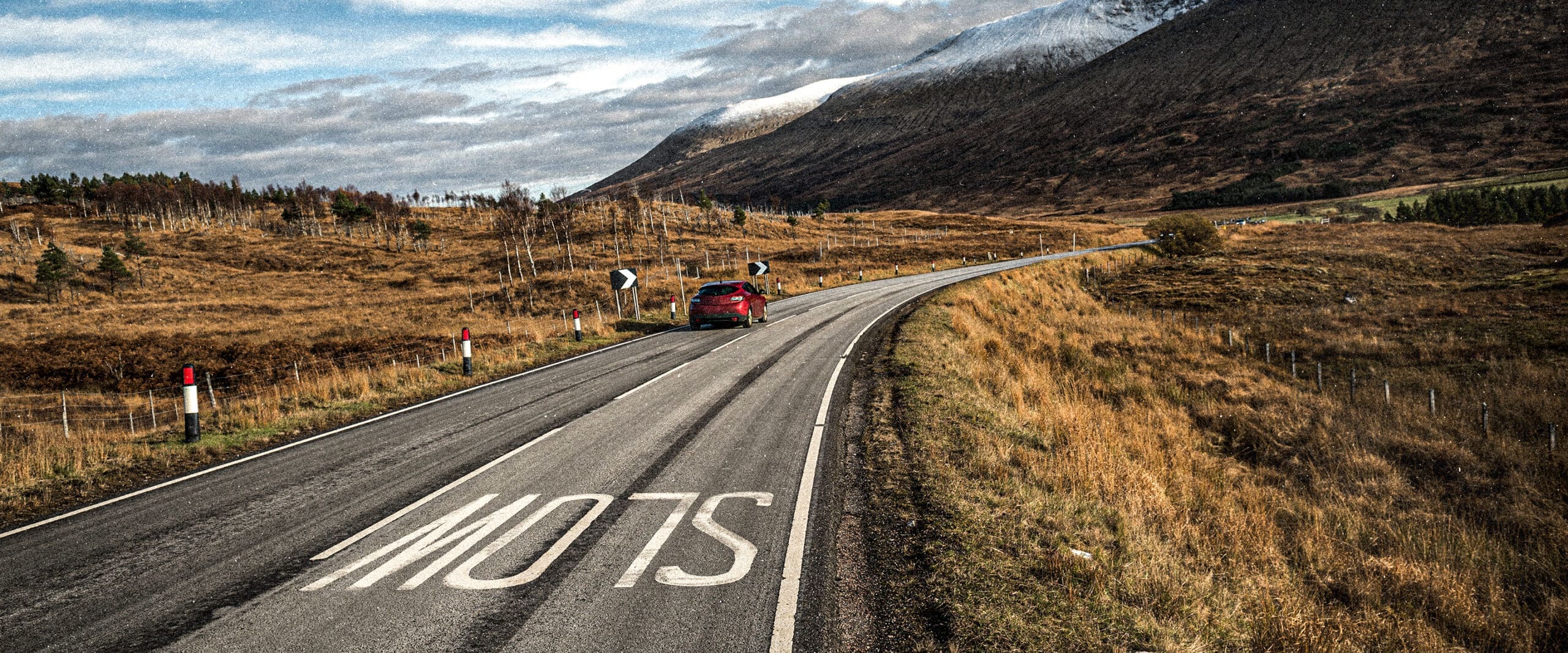 red car on left side of road -- road has "slow" written in the right lane