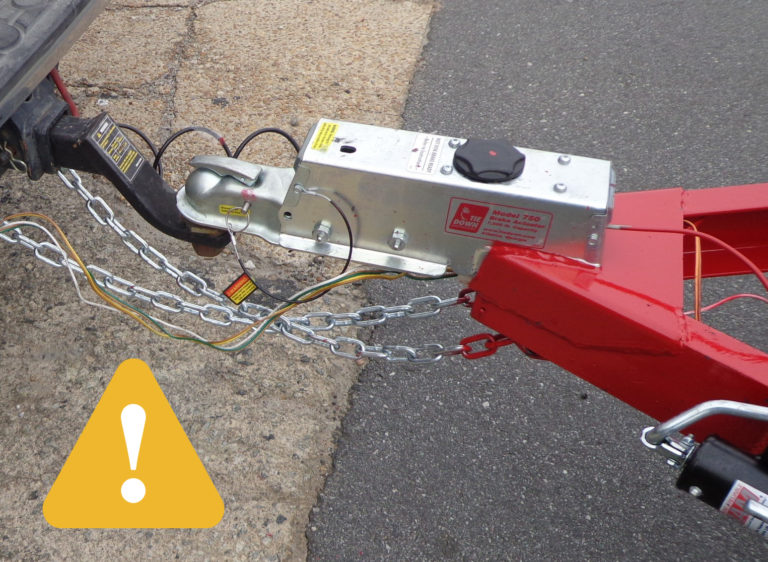 yellow caution triangle by a truck hitch and trailer hitch with safety chains connecting the two